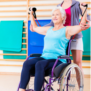 Travel Gym Portable System | Workout how you need to | Trainer assisting an elderly woman in a wheelchair doing chest presses with the Travel Gym